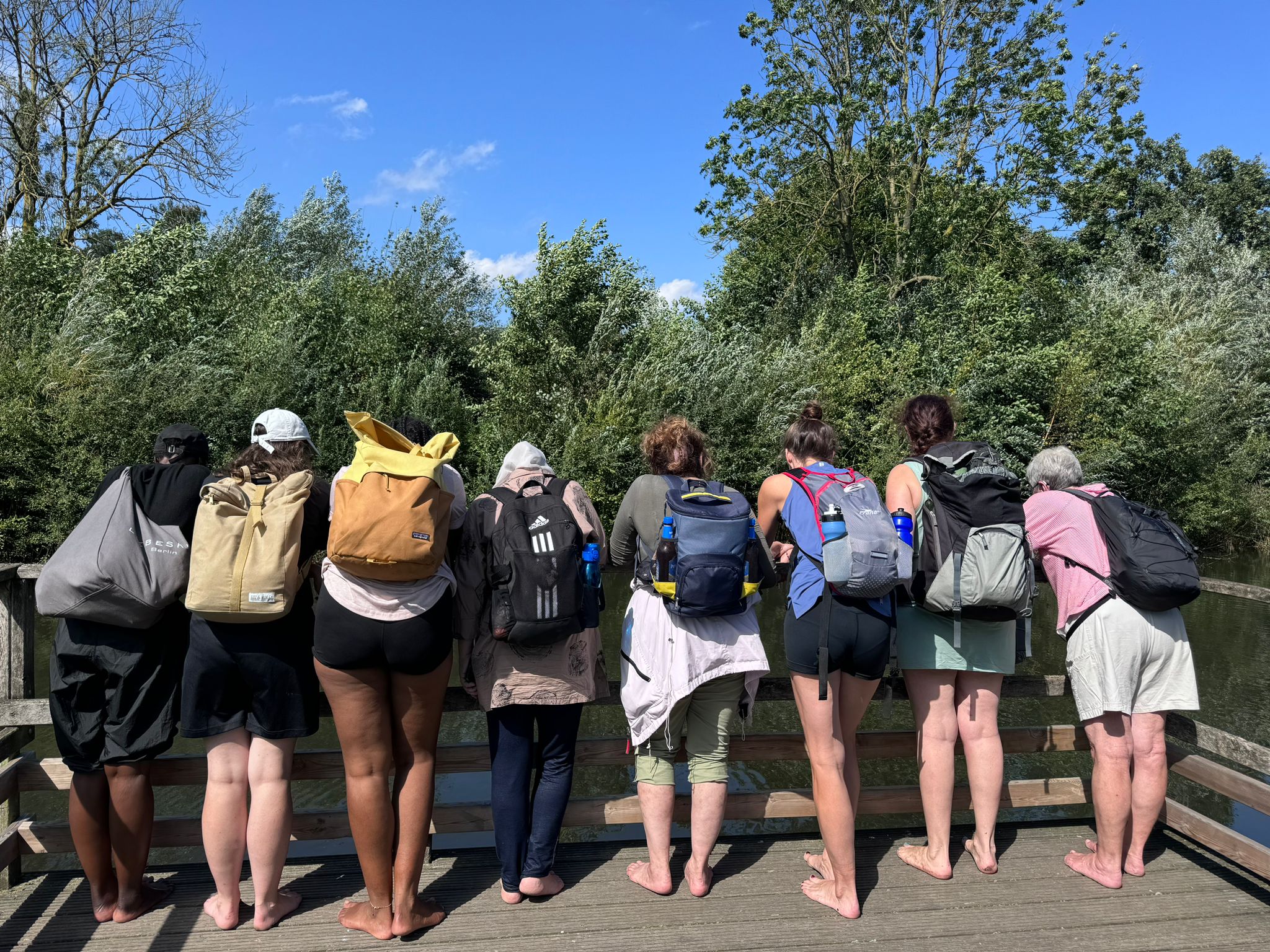 8 Frauen von Hinten mit Rucksäcken auf dem Rücken