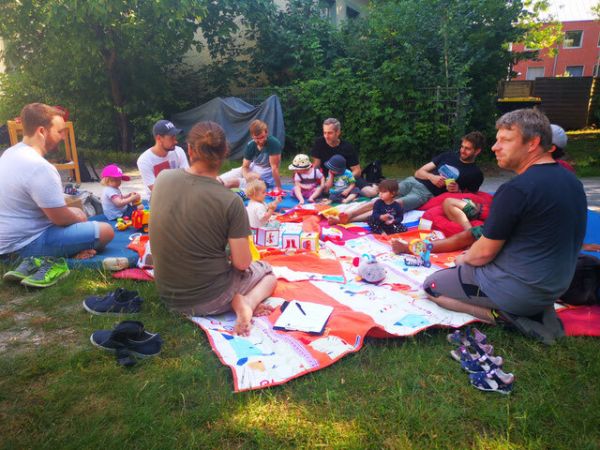 Väter mit ihren Kindern sitzen im Garten und unterhalten sich